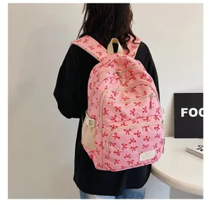 Back view of a pink schoolbag with red bow pattern on a model in a minimal room
