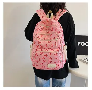 Back view of a trendy pink backpack featuring red bow patterns worn by a student
