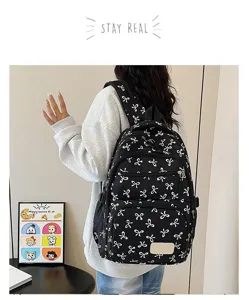 Back view of a stylish black backpack with white bow prints on a female model