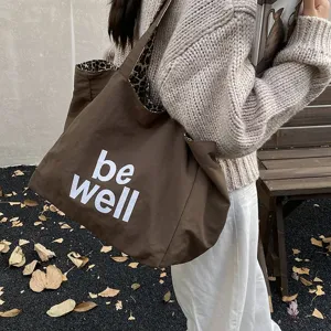 Detail of large brown canvas tote bag with 'be well' print and leopard lining