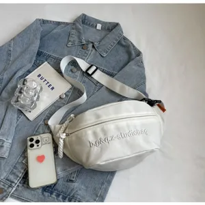 Detail view of the white sporty chest bag with studiobag embroidery on a denim jacket