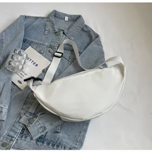 White minimalist crescent crossbody bag styled on a denim jacket with stylish lifestyle props