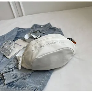 Minimalist white multi-functional chest bag with embroidered logo shown in a lifestyle setting.
