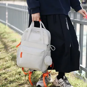 Personne tenant un sac à dos beige avec des sangles orange dans un parc à l'extérieur