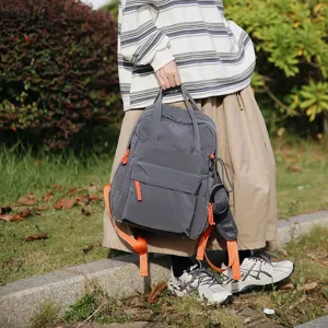 Vue lifestyle d'un sac à dos gris imperméable avec des détails orange dans un jardin
