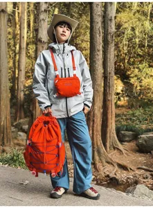 Großer orangefarbener Wanderrucksack mit Kordelzug, getragen von einem Model im Wald