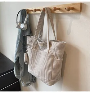 Detailed view of a beige large capacity corduroy tote bag in vintage style hanging on a wooden hook