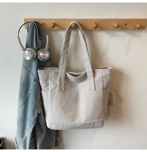 Beige corduroy tote bag hanging on a wooden rack with a denim jacket and headphones