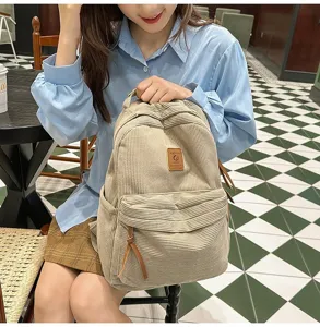 Zaino in velluto a coste beige tenuto da una modella in un caffè accogliente per il campus