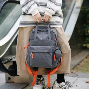 Sac à dos de banlieue gris à carreaux avec sangles oranges tenu par un mannequin