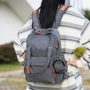 Modèle portant un sac à dos de voyage gris à carreaux avec des accents orange dehors