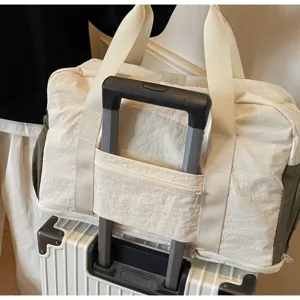 Close-up of a cream travel duffel bag attached to a rolling suitcase handle bar.