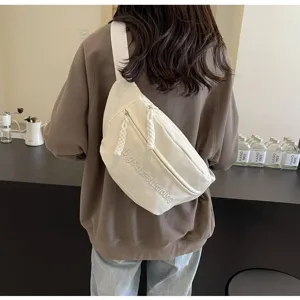 Woman wearing minimalist white canvas crossbody sling bag in modern cafe setting.