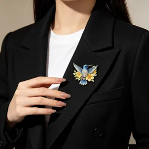 Eleganter Emaille-Kolibri-Brosche mit gelben Blumen an einem schwarzen Blazer-Jackett.