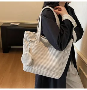 Shoulder view of a large cream corduroy tote bag with a small round pouch