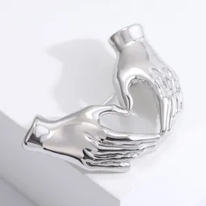 Kreative silberne Hand-Herz-Brosche mit polierter Oberfläche auf weißem Grund.