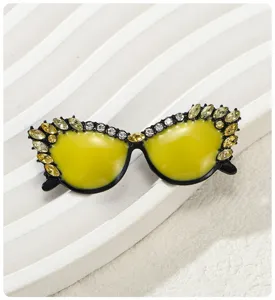 Primer plano del esmalte amarillo y los detalles de strass del broche de gafas