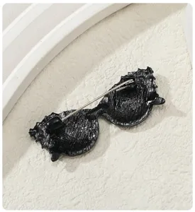Vista trasera detallada de un broche con forma de gafas de sol negras y cierre de alfiler