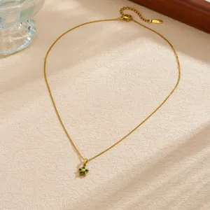Detailed view of a gold-plated flower pendant necklace with green stones on a textured background.