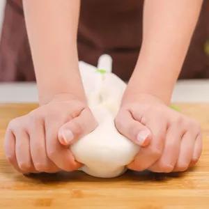 Macro view of hands kneading dough in a white food-grade silicone bag on wood board