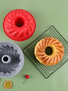 Top view of red and grey silicone bundt cake molds with a fresh baked cake on a cooling rack