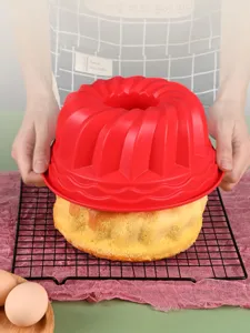 Red silicone Bundt cake mold being lifted off a freshly baked cake on a cooling rack