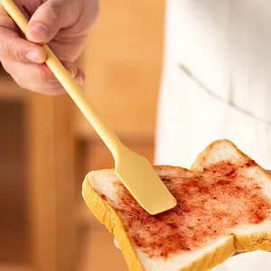 Yellow silicone jam spatula spreading fruit preserve on a slice of toasted bread.