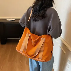 Back view of a large orange waterproof travel gym bag carried on shoulder by a model
