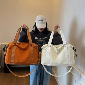 Model holding orange and off-white waterproof travel duffel bags for gym and sports.