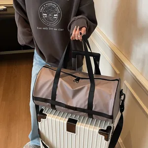 Grande borsa da viaggio taupe tenuta da una modella sopra una valigia bianca lucida
