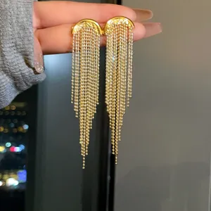 Close-up detail of gold-plated long tassel earrings with delicate ball chain fringe.