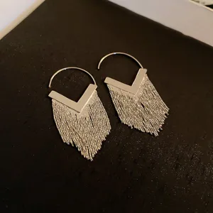 Close-up of silver-tone hoop earrings with long metallic fringe and V-shaped detail.