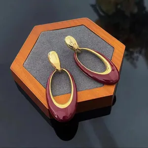 Close-up shot of elegant burgundy red and gold oval drop earrings on a wooden display stand