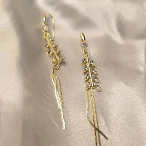Close-up of elegant gold wheat stalk earrings with zircon stones and long tassels