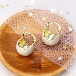 Detail shot of vintage white enamel hoop earrings with gold interior on a wooden plate.