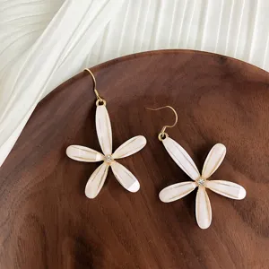Detailed view of white five-petal flower earrings with gold accents and crystal centers