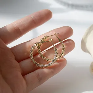 Macro detail of elegant gold textured hoop earrings held in hand under soft natural light