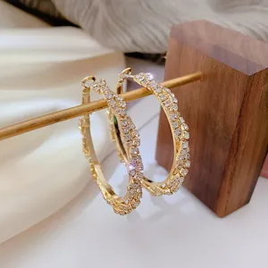 Close-up of sparkling gold crystal hoop earrings displayed on a rustic wooden stand