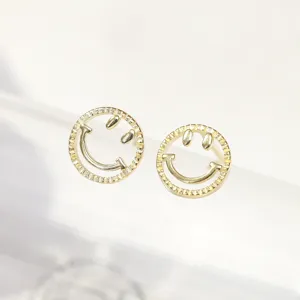 Macro detail of fashionable golden smiley face stud earrings with textured outer rims