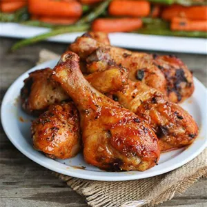 Delicious grilled chicken drumsticks served on a white plate with rustic background
