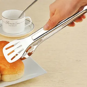 Nahaufnahme von Küchenzange aus Edelstahl, die ein frisch gebackenes Brötchen greift