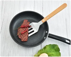 Close-up view of a stainless steel BBQ spatula with a wooden handle flipping steak in a pan.