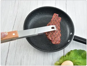 Detailed view of stainless steel BBQ tongs with wooden handle flipping a steak in a pan