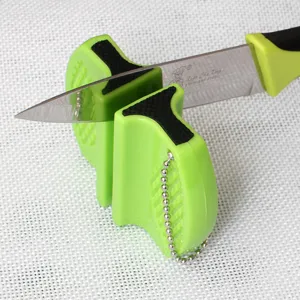Close-up of a mini portable knife sharpener in green being used on a stainless steel blade.