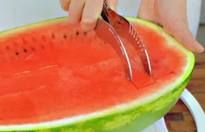 Action shot showing a stainless steel watermelon slicer tool cutting juicy red fruit