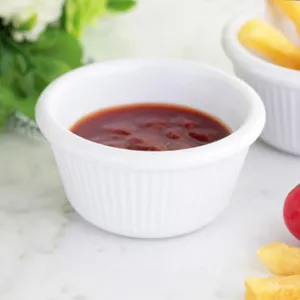Close-up of white ribbed ceramic sauce bowl filled with ketchup on marble table