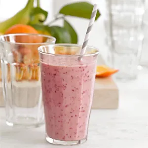 Close-up of fresh pink berry smoothie served in a transparent octagonal acrylic cup with a straw