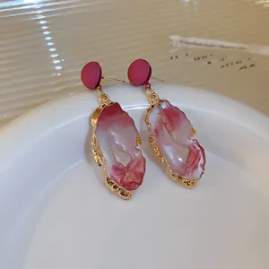 Close-up of elegant red marbled resin earrings with textured gold-tone edges for women.