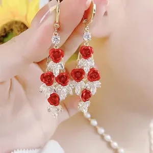Elegant gold-tone long drop earrings with red rose charms and sparkling white crystals