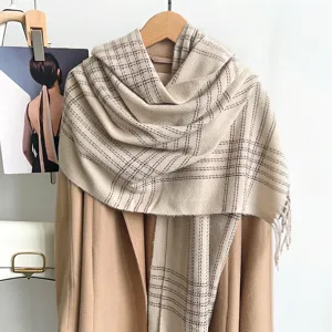 Détail d'une écharpe à carreaux beige à pompons drapée élégamment sur un manteau d'hiver beige